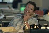 A film still of Matt Damon, a middle-aged man, sits at a desk smiling brightly, holding a rotary phone receiver to his ear.