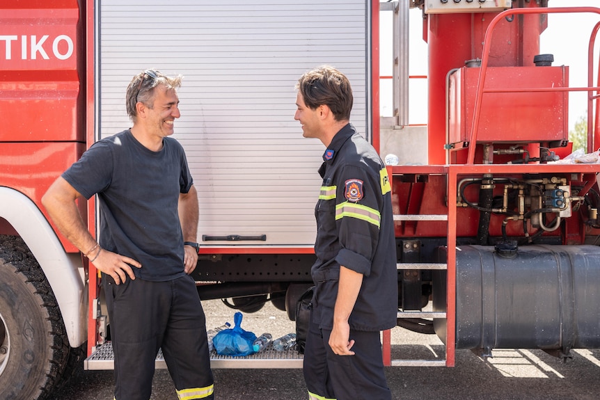 Two men in firefighter gear standing next to a red truck