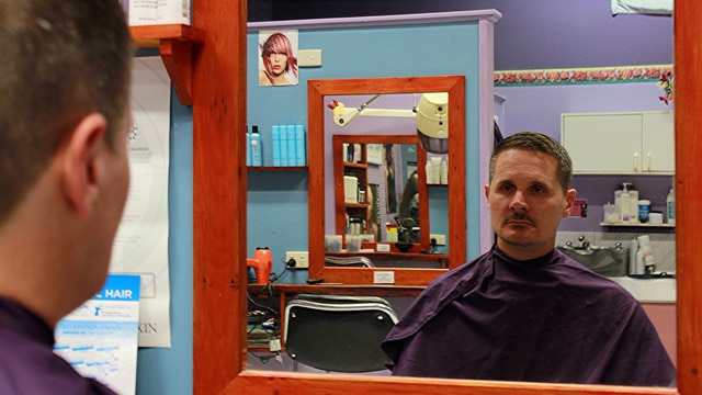 A man in a barber's chair reflected in the mirror