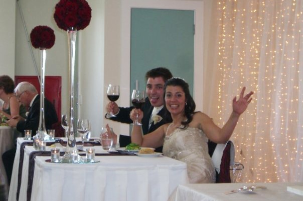 A married couple toasting the camera at their wedding reception.