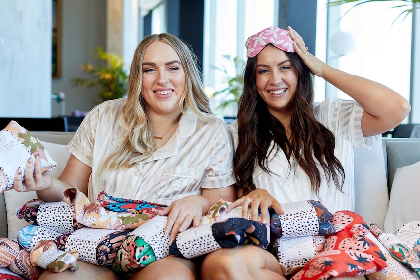 two women wearing pyjamas surrounded by heat packs smiling at the camera