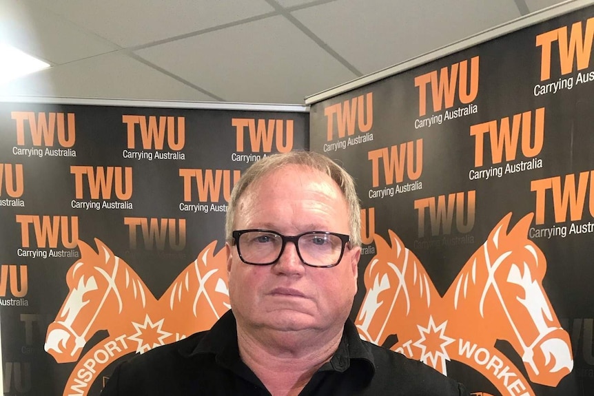 A man stands with his hands on his hips in front of a TWU banner