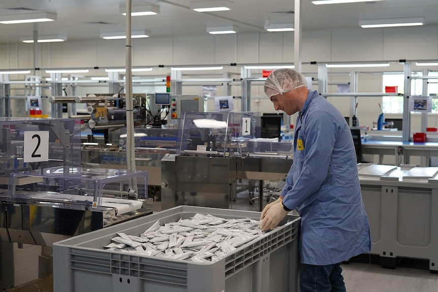 Scientist in lab coat and hair net stands next to bin of COVID-19 tests.