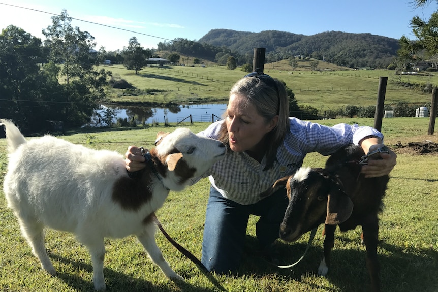 Sally Hookey crouches down between her miniature goats, blowing a kiss at one of them.