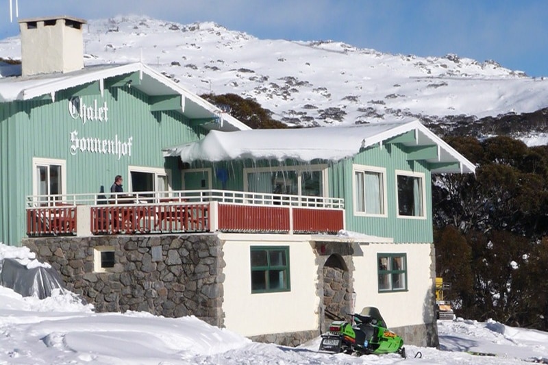 A ski lodge on a hill with a snow-covered mountain in the background.