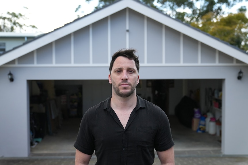 A man with short dark hair looks into the camera with a serious expression on his face.