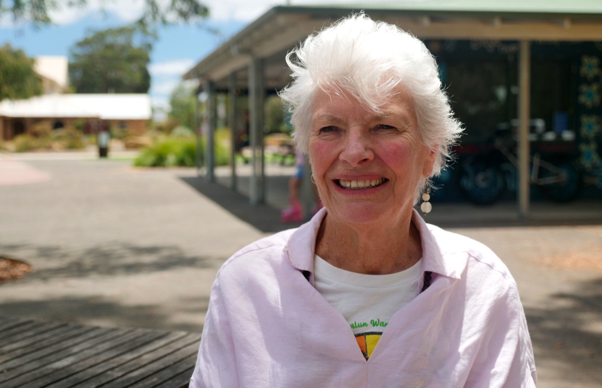 Una mujer con una camisa rosa se encuentra frente a un edificio. 