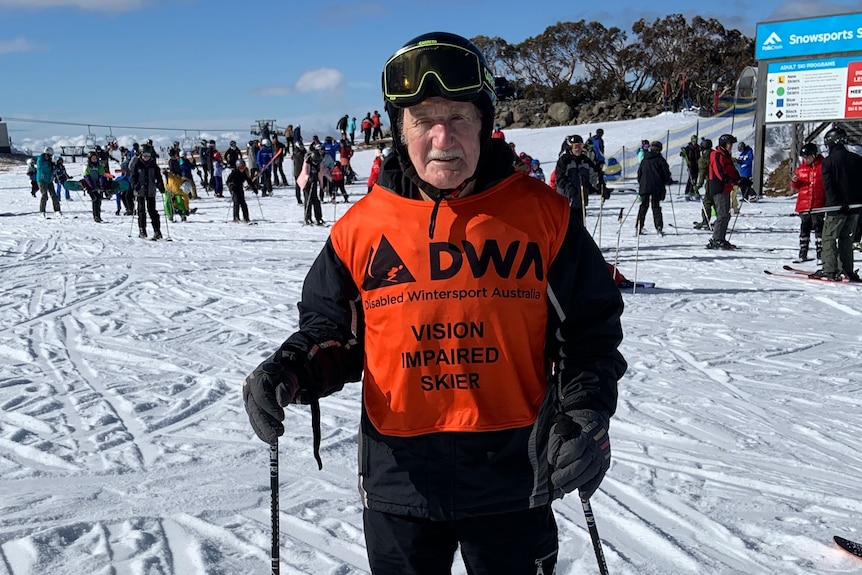 A man wearing a vest that says vision impaired, in the snow with skis