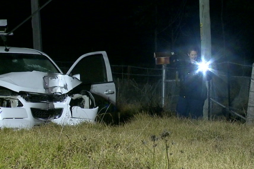 A woman with a torch near a smashed car.