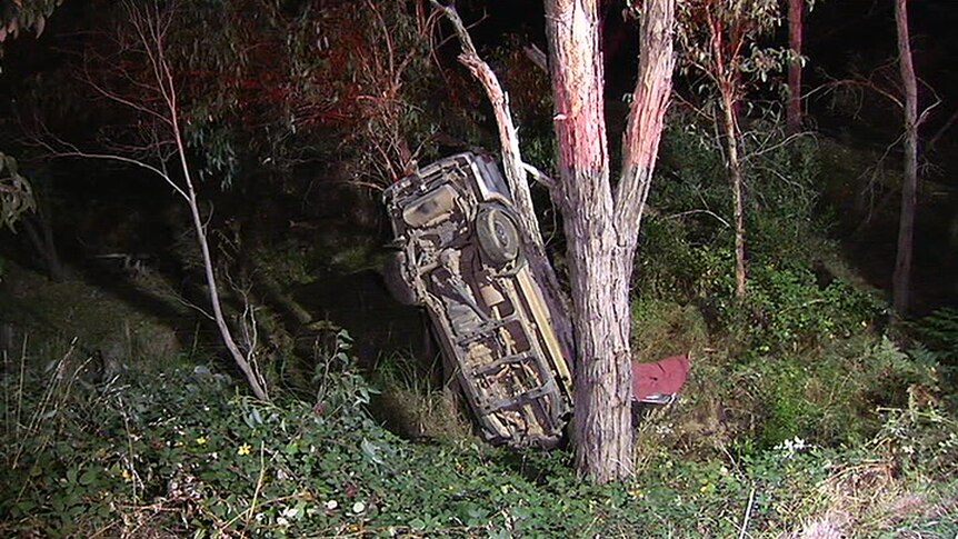 A car flipped and standing on its nose lies against a tree, following a fatal car crash at Dixons Creek.