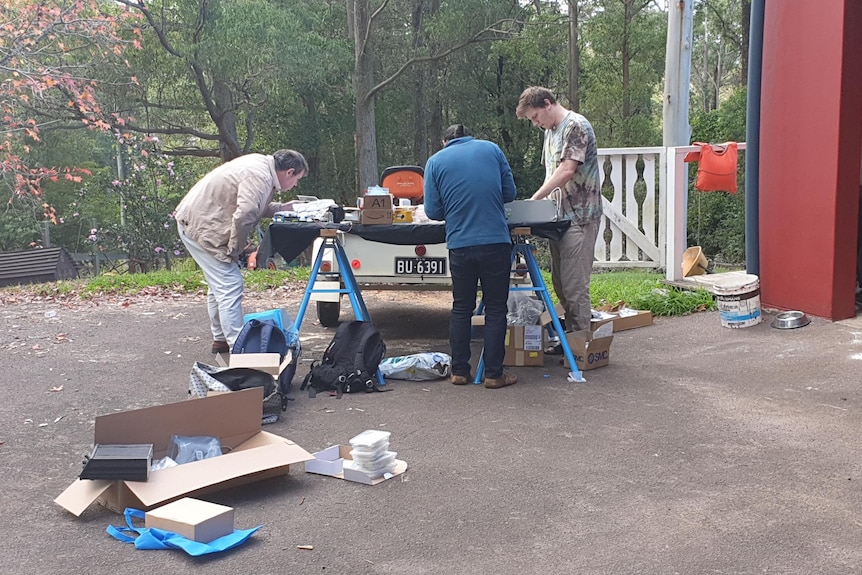 Three people work around a table on a driveway.