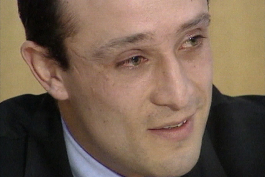 A close up of a man's face as he looks to the side. He is wearing a suit.