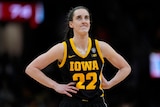 A female college basketball player stands with her hands on hips, looking concerned during a final