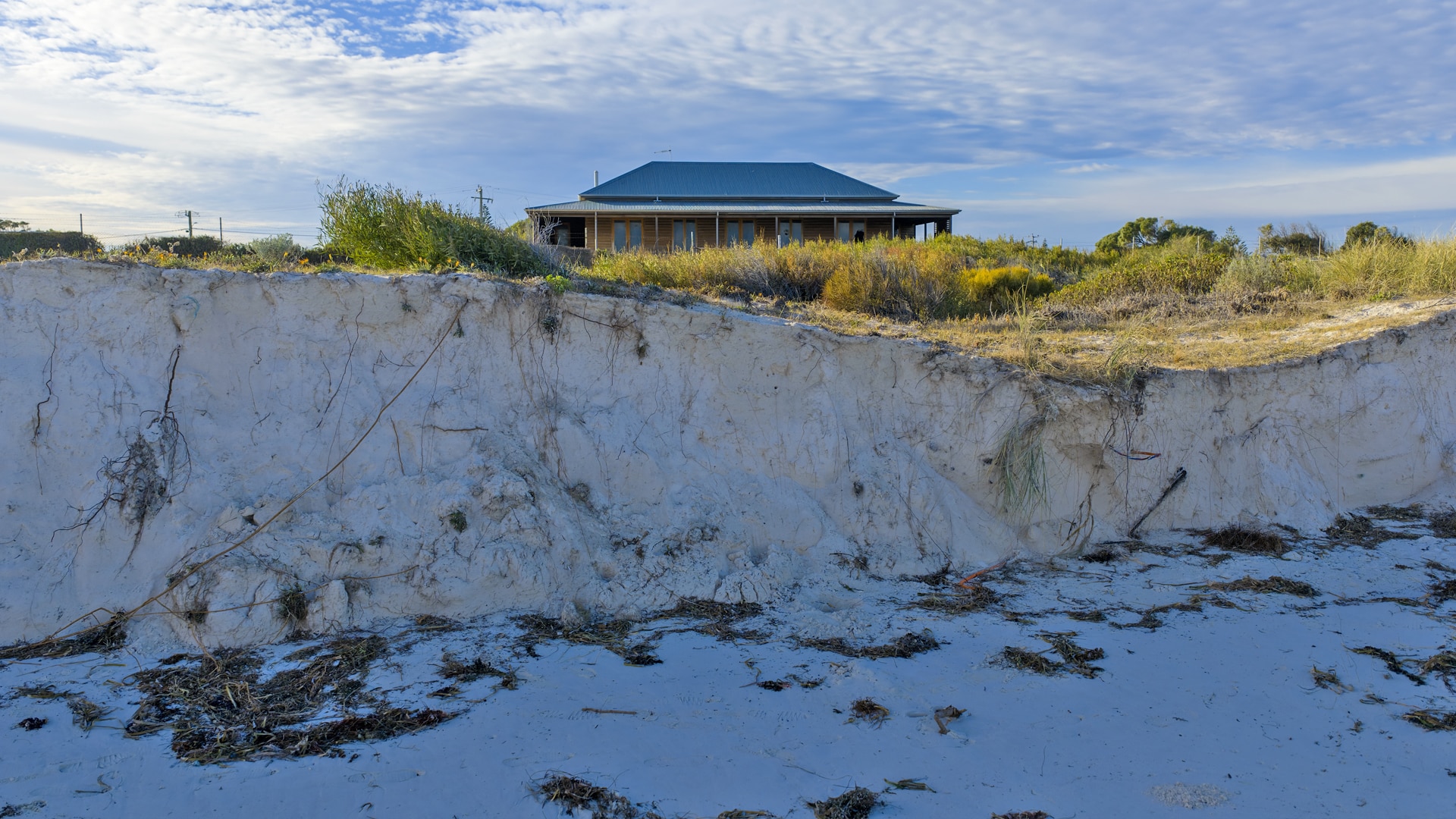 A steep drop in a sand dune, with a house in the background.