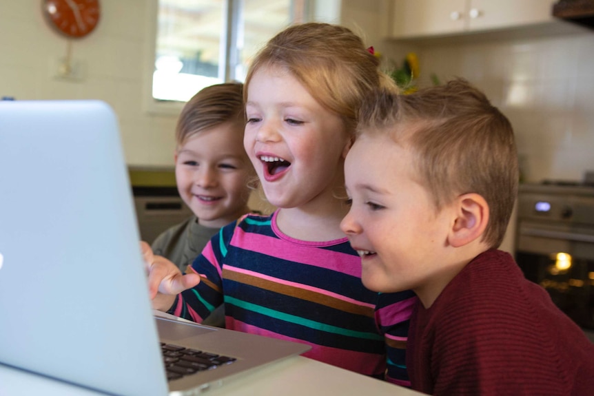 A group of young children smile as they look at a computer screen.