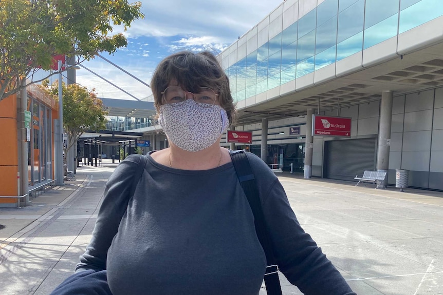 A woman outside Brisbane airport carrying a bag and wearing a flu mask