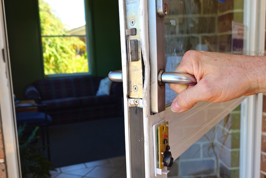 A man's hand holding a door handle with a slightly dented lock. 