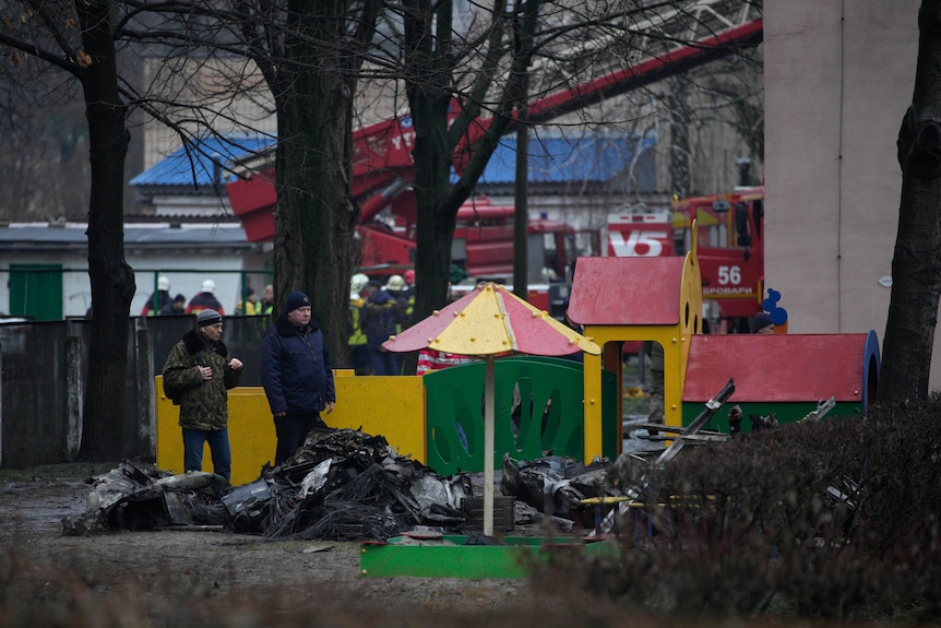 A children's playground has debris around it and a crane after a helicopter crash.