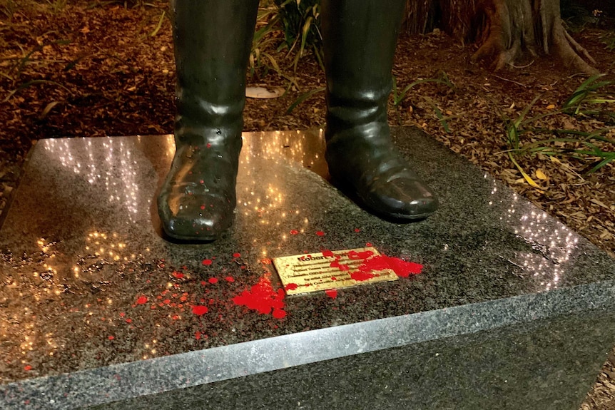 The mantle of a statue, whose feet are visible. The mantle and the plaque it bears are marked with drops of red paint.