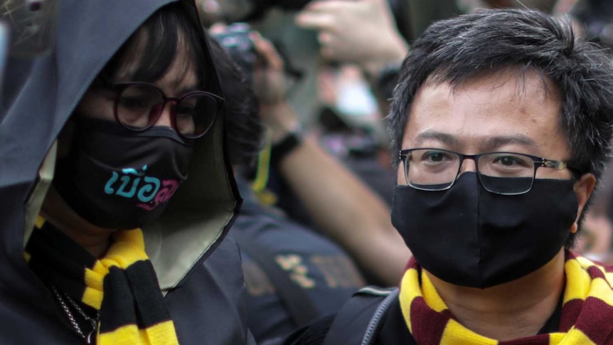 Two young men are dressed in black gowns and wearing yellow and maroon scarves. One man is looking at the other
