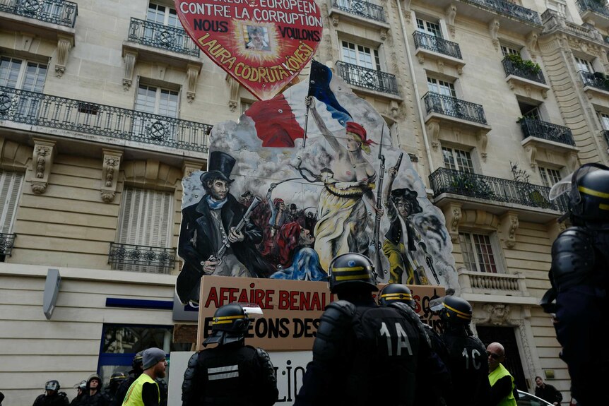 A large poster imitating a French revolution painting with police in riot gear standing underneath.