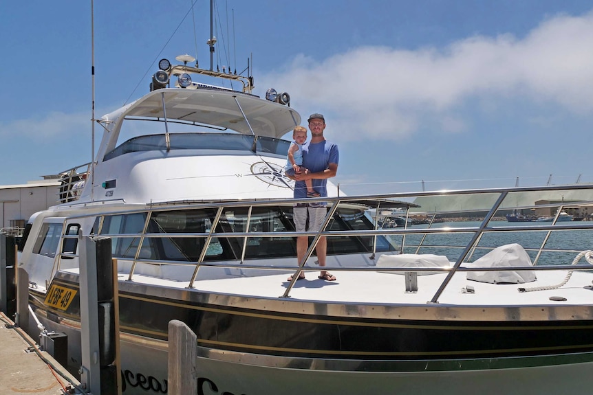 Jake Suckling stands on the bow of his fishing boat while holding his 19-month-old son Hale.