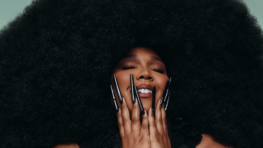 A woman with very long black fingernails holds her hands to her face