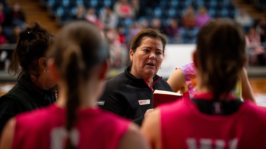 A woman in a dark shirt speaking to Netbal players in red shirts.