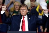 A man holds his fists aloft and looks at a large crowd as he speaks to them inside a venue.