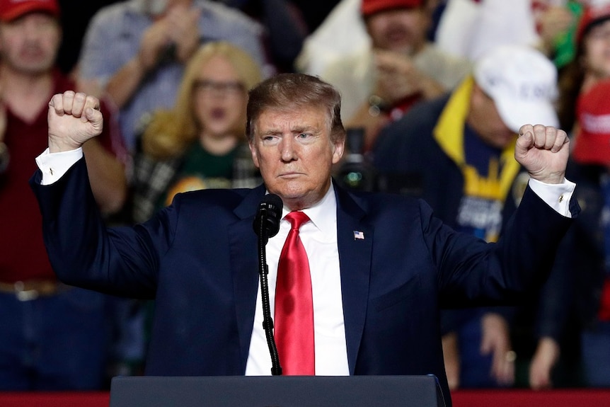 A man holds his fists aloft and looks at a large crowd as he speaks to them inside a venue.