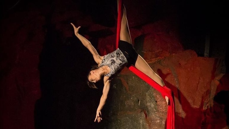 Gymnast coach and circus performer Anna McGoldrick upside down in circus silks in front of a rock wall