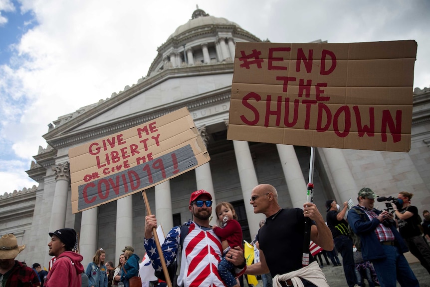 A crowd of people stand on the steps of a grand building, some of them holding signs