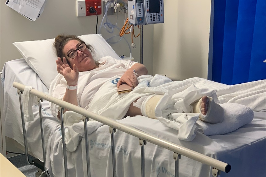 A middle aged woman lies in a hospital bed with a cast on her right foot