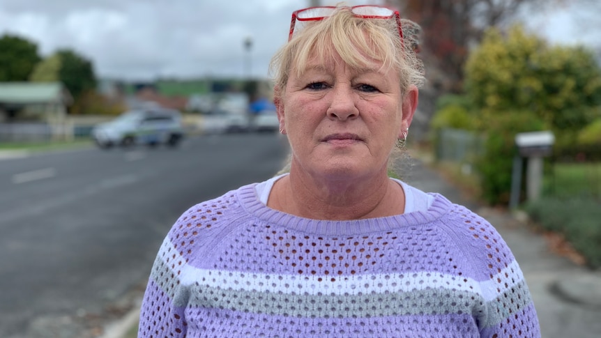 A middle aged woman in a jumper stands on a street