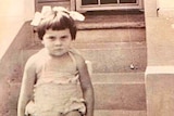 A young girl sitting on a step looks straight into the camera.