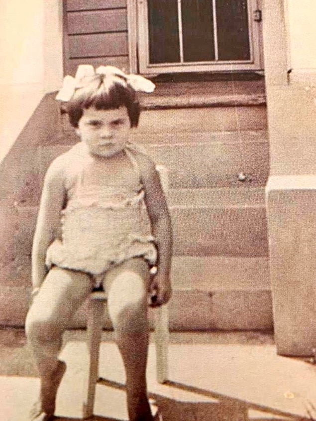A young girl sitting on a step looks straight into the camera.