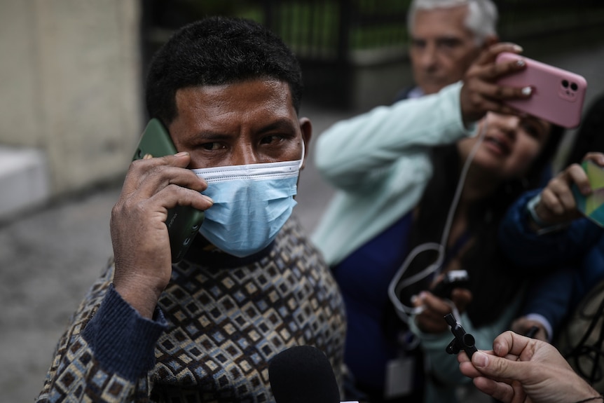 A Colombian man wearing a mask and holding a mobile phone to his ear at a press conference