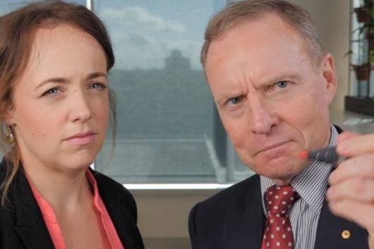 Woman glaring with David Morrison next to her looking serious, holding pen