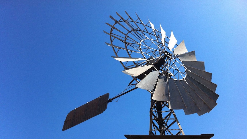 A silver metal windmill against bright blue sky