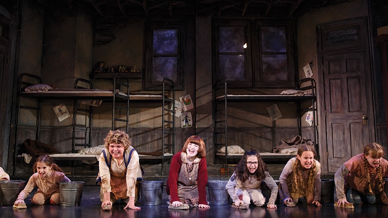 A group of children scrub the floor in a musical production of Annie. 