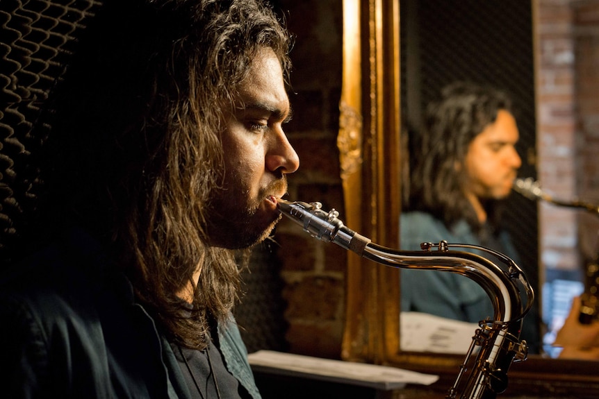 Amoody shot of a man playing a saxaphone.