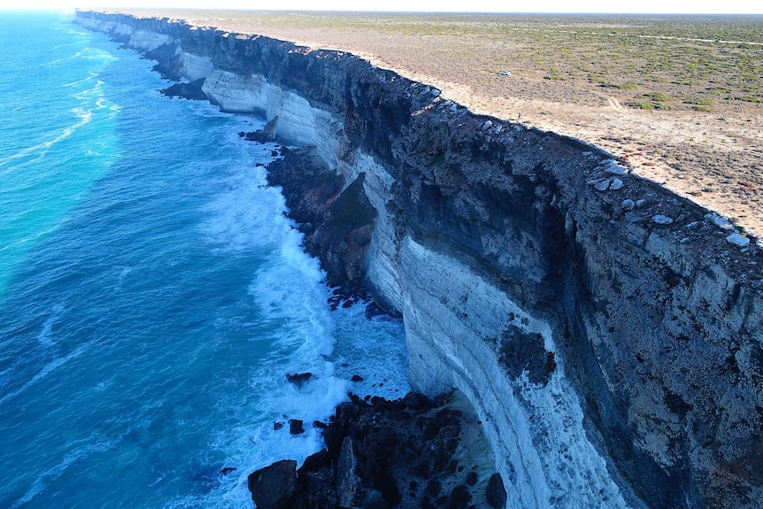 Tall cliffs with ocean waves and tiny person and vehicle on top