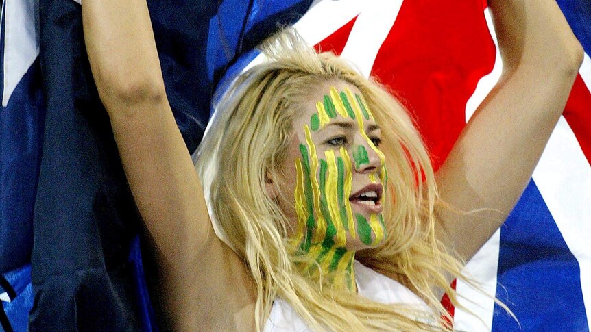 Lauren Jackson waves an Australian flag over her head while wearing green and gold paint on her face.