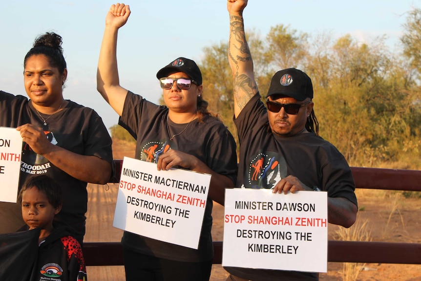 Group stands on a bush road, raise fist in air, hold placards, saying minister Dawson stop Shangai Zenith destroying Kimberley.