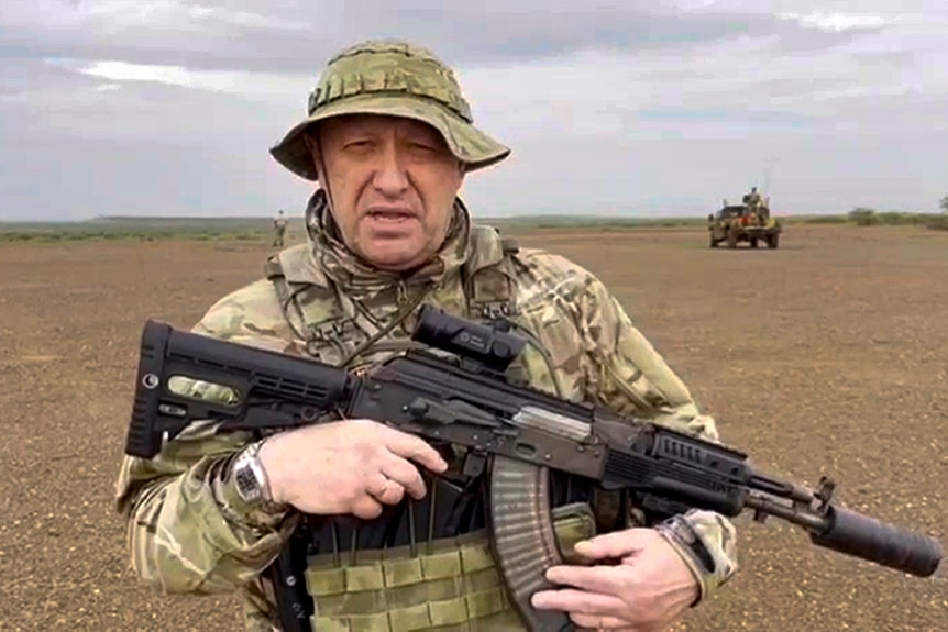 Yevgeny Prigozhin stands in an open plain holding a gun.