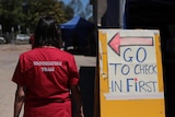 A person with a 'Vaccination team' red t-shirt is seen standing next to a check-in signage.