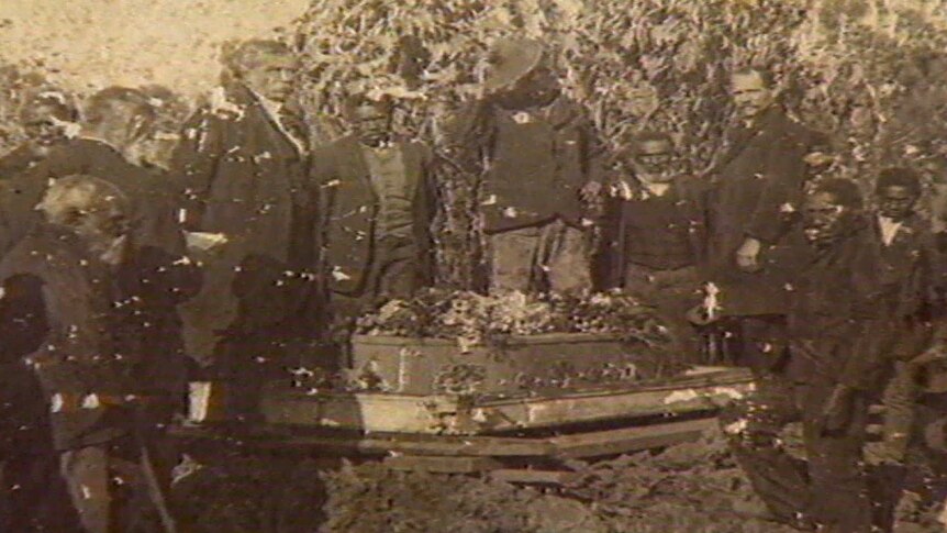 South Sea Islander men gather around a coffin which is ready to be buried