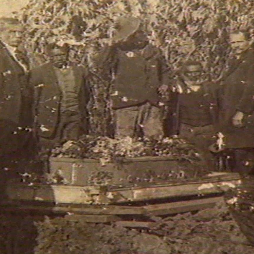 South Sea Islander men gather around a coffin which is ready to be buried