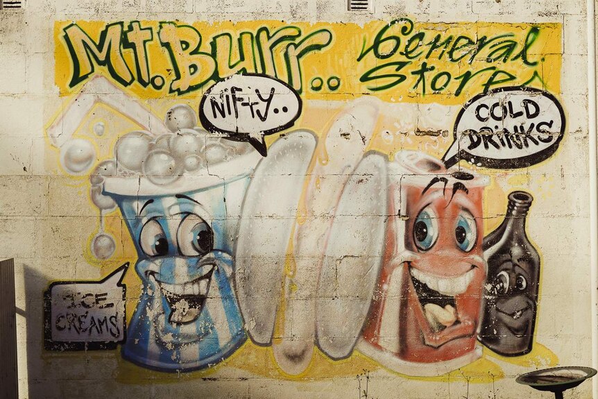 A mural with the words 'Mt Burr General Store' painted in green and yellow with two cartoon smiling soda cans below it.