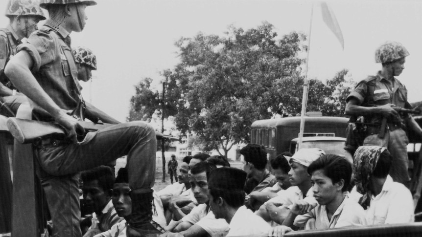 A soldier points a weapons at young men in the back of a truck